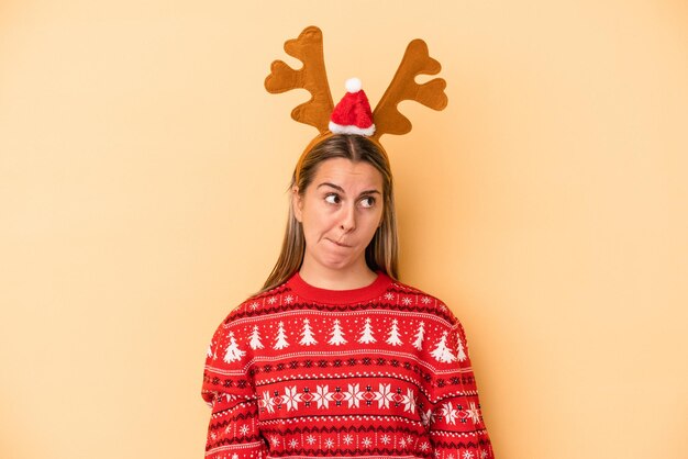 Una joven caucásica con un sombrero de reno de navidad aislado en un fondo amarillo confundida, se siente dudosa e insegura.