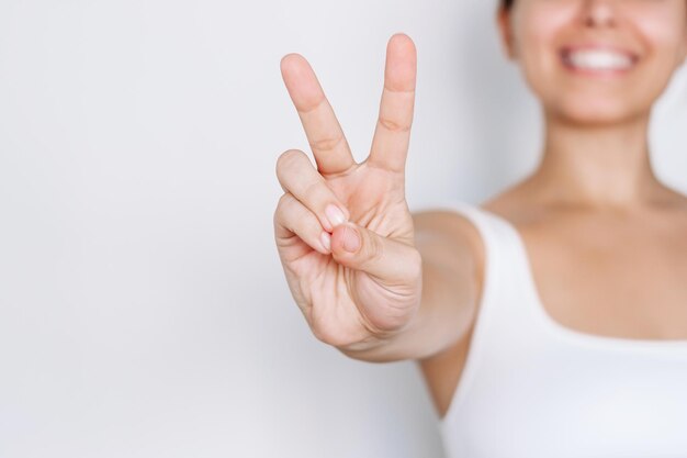 Foto una joven caucásica sonriente y alegre con un top blanco mostrando un gesto de paz con la mano