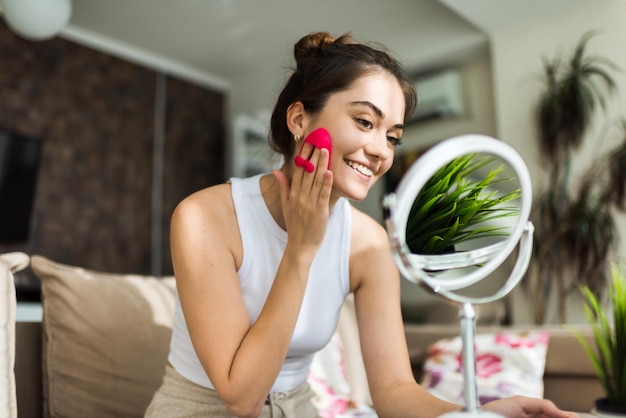 Foto una joven caucásica sonriente está haciendo un masaje facial mirándose en el espejo