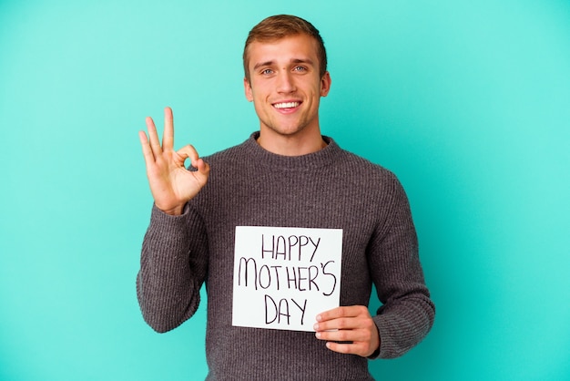 Joven caucásica sosteniendo un feliz día de las madres aislado sobre fondo azul.