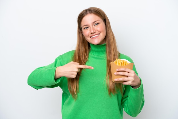 Joven caucásica sosteniendo patatas fritas aisladas de fondo blanco y señalándola