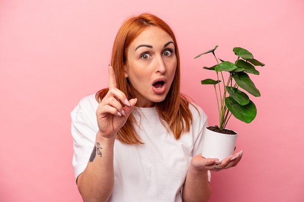 Joven caucásica sosteniendo una planta aislada sobre fondo rosa Joven caucásica sosteniendo una planta aislada sobre fondo rosa con un concepto de inspiración de idea