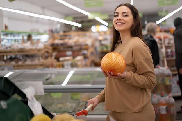 Una joven caucásica en un supermercado compra un pomelo Una mujer compra comestibles y productos básicos en una tienda orgánica local