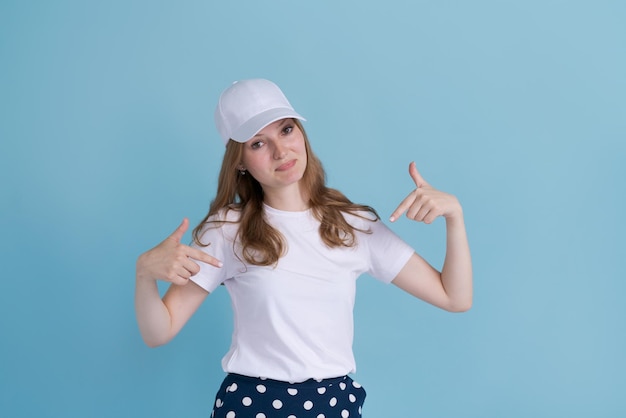 Joven caucásica con uniforme de entrega y gorra blanca se ve confiada con una sonrisa en la cara señalando...