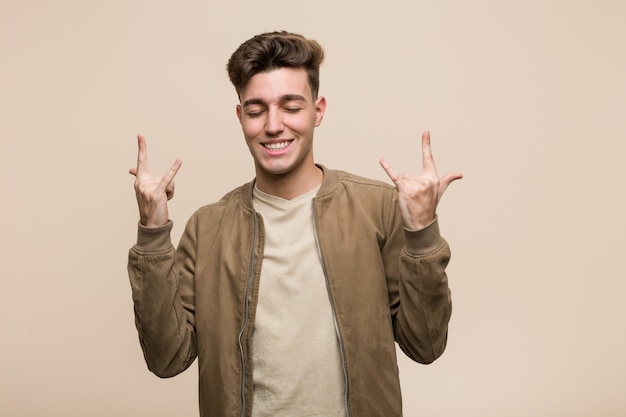 Joven caucásica vistiendo una chaqueta marrón mostrando gesto de rock con los dedos