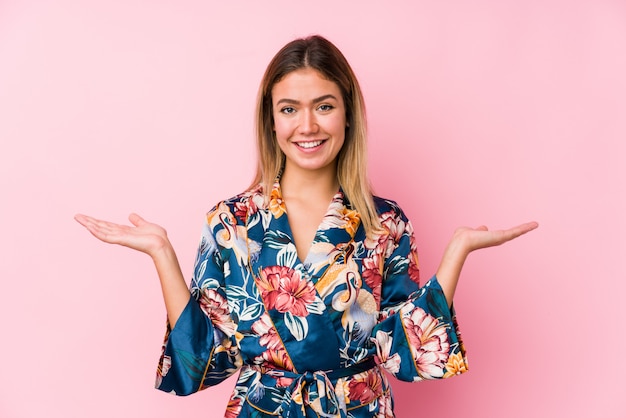 Joven caucásica vistiendo pijama hace escala con los brazos, se siente feliz y confiada.