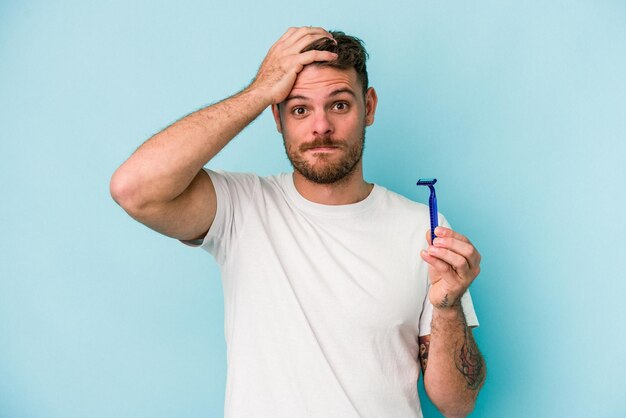 Un joven caucásico afeitándose la barba aislado de fondo azul se sorprendió, recordó una reunión importante.