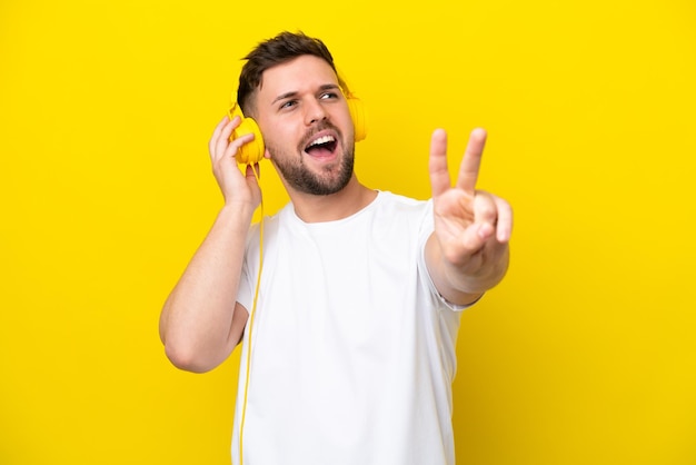 Joven caucásico aislado de fondo amarillo escuchando música y cantando