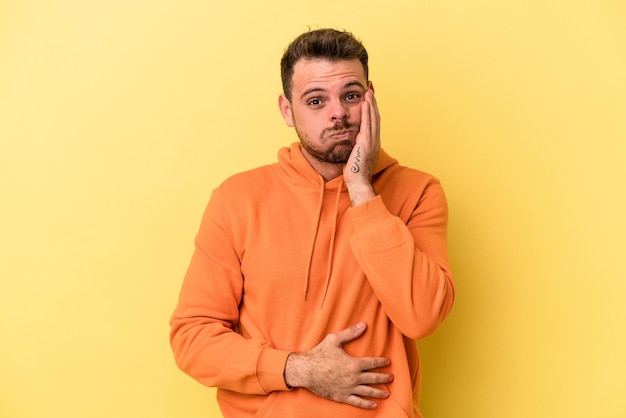 Joven caucásico aislado de fondo amarillo sopla mejillas, tiene expresión cansada. Concepto de expresión facial.