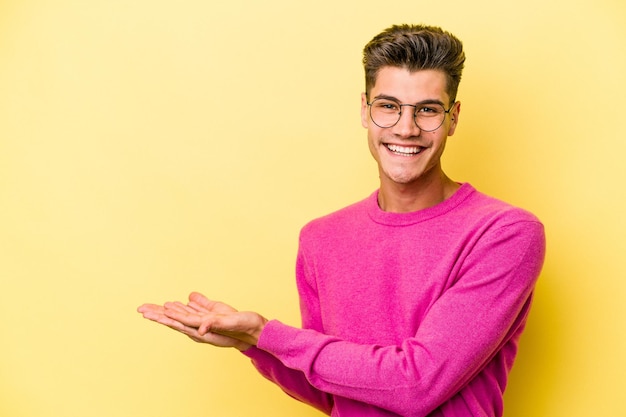 Joven caucásico aislado de fondo amarillo sosteniendo un espacio de copia en una palma.