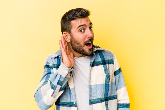 Joven caucásico aislado de fondo amarillo tratando de escuchar un chisme