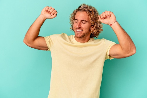 Joven caucásico aislado de fondo azul celebrando un día especial, salta y levanta los brazos con energía.