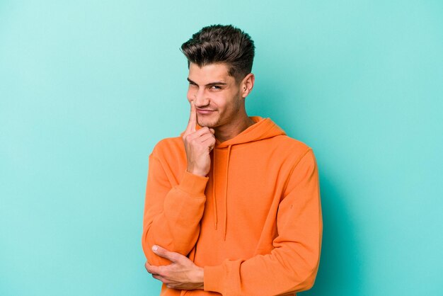 Joven caucásico aislado de fondo azul contemplando la planificación de una estrategia pensando en el camino de un negocio