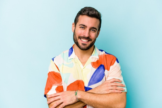 Joven caucásico aislado de fondo azul que se siente confiado cruzando los brazos con determinación