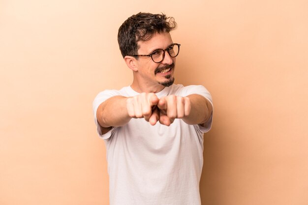 Joven caucásico aislado de fondo beige apuntando al frente con los dedos