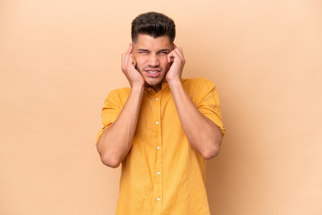 Joven caucásico aislado de fondo beige frustrado y cubriendo las orejas