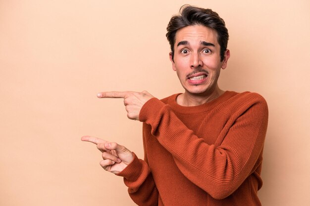 Joven caucásico aislado de fondo beige sorprendido señalando con el dedo índice a un espacio de copia