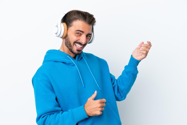 Joven caucásico aislado de fondo blanco escuchando música y haciendo gestos de guitarra