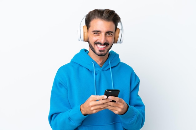 Joven caucásico aislado de fondo blanco escuchando música con un móvil y mirando al frente