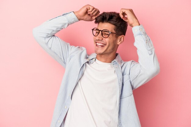 Joven caucásico aislado de fondo rosa celebrando un día especial, salta y levanta los brazos con energía.