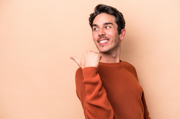 Joven caucásico aislado en puntos de fondo beige con el dedo pulgar lejos riendo y despreocupado