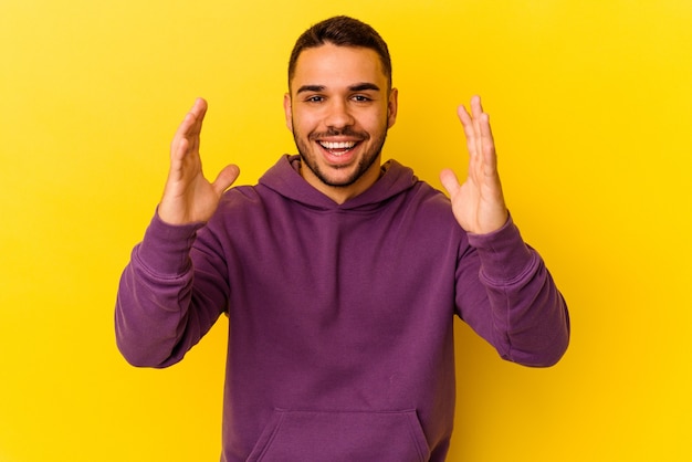 Joven caucásico aislado sobre fondo amarillo recibiendo una agradable sorpresa, emocionado y levantando las manos.