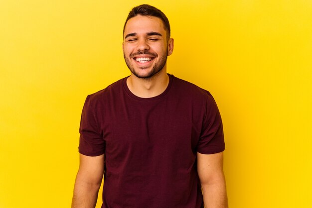 Joven caucásico aislado sobre fondo amarillo se ríe y cierra los ojos, se siente relajado y feliz.