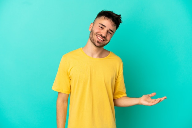 Joven caucásico aislado sobre fondo azul presentando una idea mientras mira sonriendo hacia