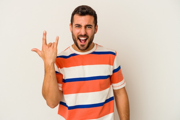 Joven caucásico aislado sobre fondo blanco mostrando gesto de rock con los dedos