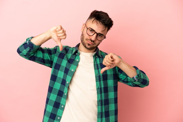 Foto joven caucásico aislado sobre fondo rosa mostrando el pulgar hacia abajo con las dos manos