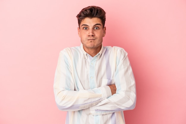 Joven caucásico aislado sobre fondo rosa sopla mejillas, tiene expresión cansada. Concepto de expresión facial.