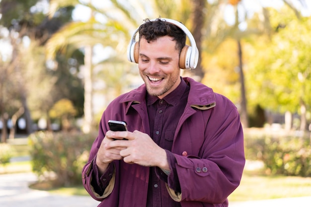 Joven caucásico al aire libre escuchando música y mirando al móvil