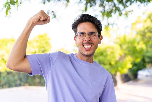 Joven caucásico al aire libre en un parque haciendo un gesto fuerte