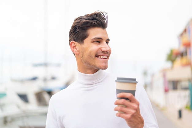 Joven caucásico al aire libre sosteniendo un café para llevar con expresión feliz