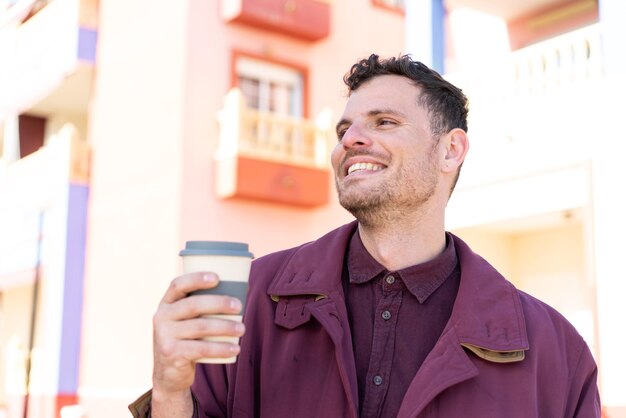 Joven caucásico al aire libre sosteniendo un café para llevar con expresión feliz