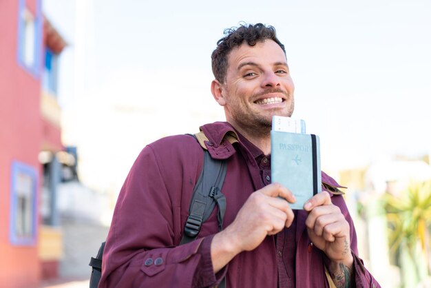 Joven caucásico al aire libre sosteniendo un pasaporte con expresión feliz