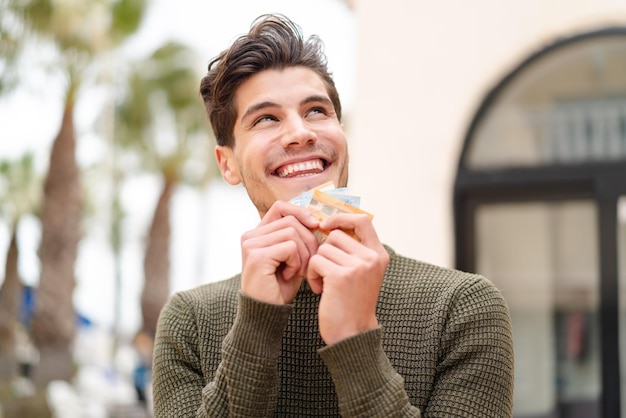 Joven caucásico al aire libre tomando mucho dinero y mirando hacia arriba