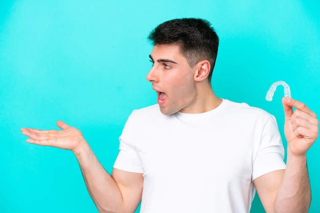 Joven caucásico con aparatos invisibles aislados en fondo azul con expresión facial sorpresa