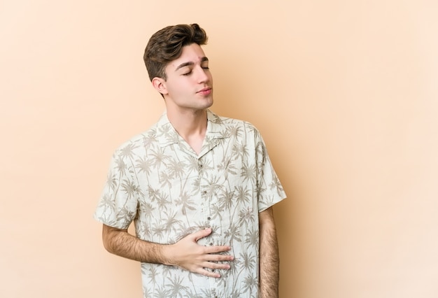 Joven caucásico en beige toca la barriga, sonríe suavemente, comiendo y concepto de satisfacción.