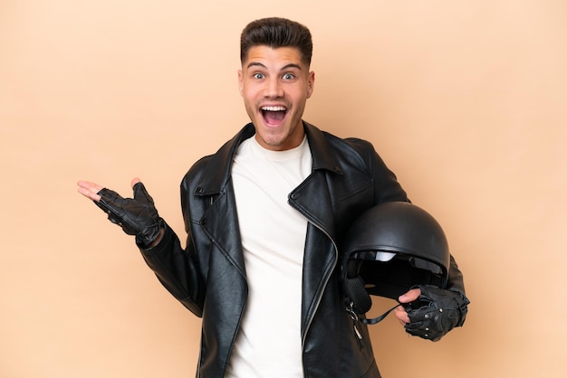 Joven caucásico con casco de motocicleta aislado de fondo beige con expresión facial conmocionada