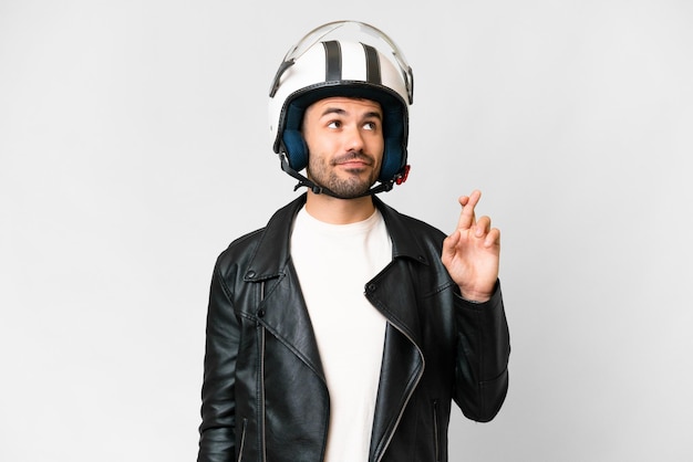 Joven caucásico con casco de motocicleta sobre fondo blanco aislado con los dedos cruzados y deseando lo mejor