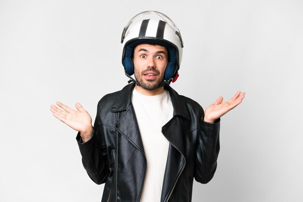 Joven caucásico con casco de motocicleta sobre fondo blanco aislado con expresión facial conmocionada