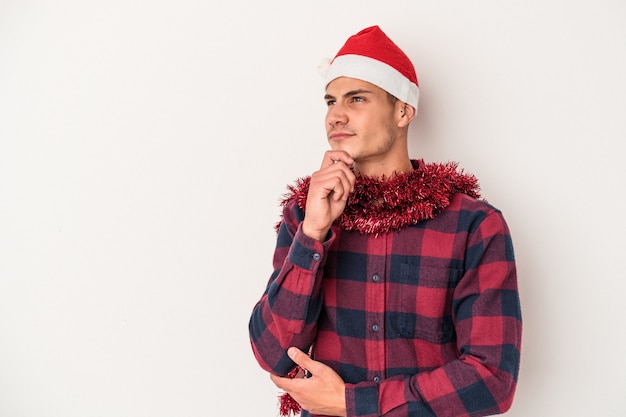 Joven caucásico celebrando la Navidad aislado sobre fondo blanco mirando hacia los lados con expresión dudosa y escéptica.