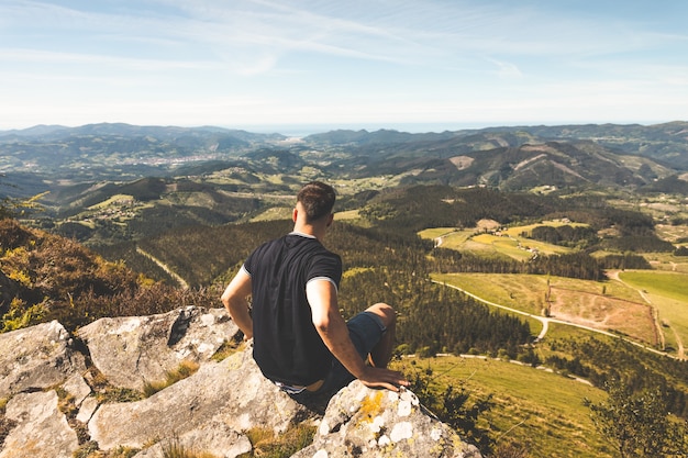 Joven caucásico en la cima de la montaña de Oiz con impresionantes vistas de todo el verde País Vasco.