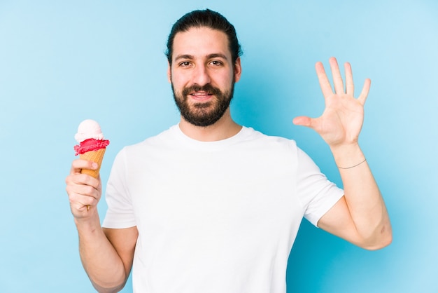 Joven caucásico comiendo un helado aislado sonriendo alegre mostrando el número cinco con los dedos.