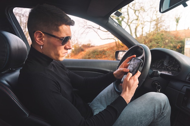 Joven caucásico dentro de un coche con un teléfono inteligente