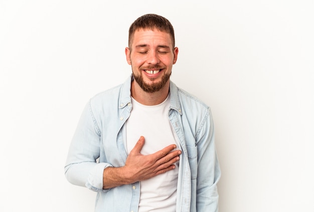 Joven caucásico con diastema aislado sobre fondo blanco se ríe a carcajadas manteniendo la mano en el pecho.