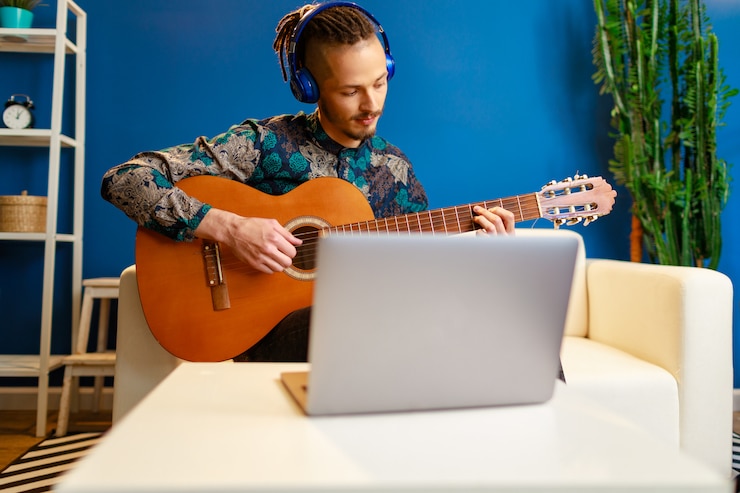 Foto joven caucásico elegante tomando clases de guitarra en línea en casa usando su portátil