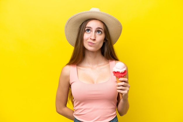 Joven caucásico con un helado de cucurucho aislado de fondo amarillo y mirando hacia arriba