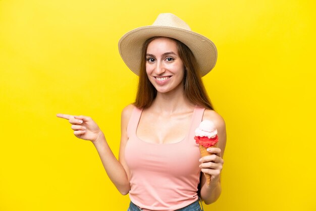 Joven caucásico con un helado de cucurucho aislado en un fondo amarillo señalando con el dedo hacia un lado